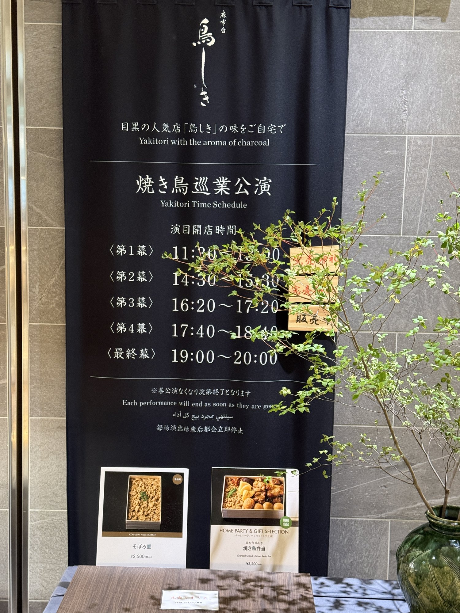 麻布台鳥しきの店頭に掲げられた「目黒の人気店『鳥しき』の味をご自宅で」というバナー。焼き鳥の巡業公演スケジュールも記載されている