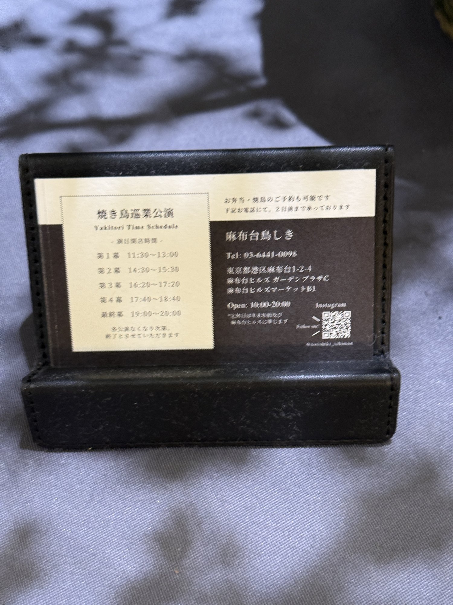 麻布台鳥しきの店舗情報が記された革製カードスタンド。住所・電話番号・営業時間・InstagramのQRコードが掲載されている